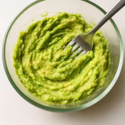 Bol en verre contenant de l’avocat écrasé avec une fourchette.